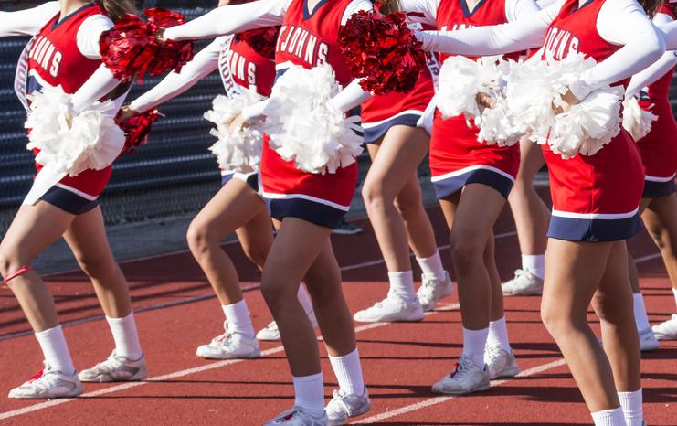 Gruppendarstellung von Cheerleadern in roten und weißen Uniformen, die auf einer Laufbahn tanzen und Pompons schwenken.